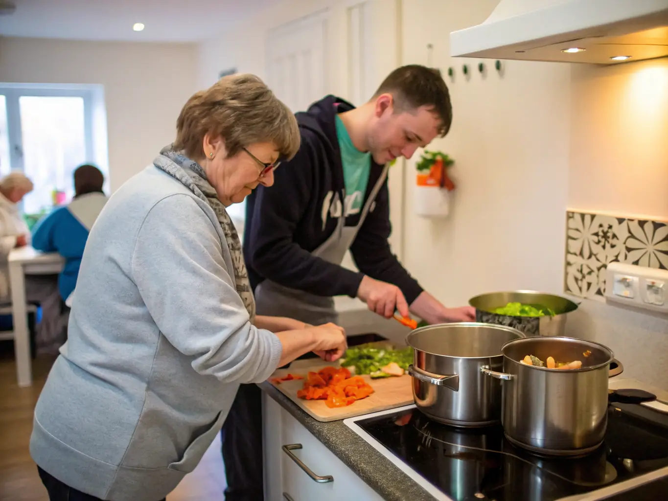 A friendly personal support worker assisting a young adult with daily living skills in a bright, homely supported living environment, both smiling and engaged in conversation.